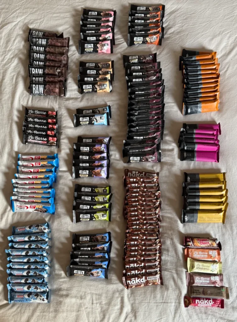 Shop-bought protein bars from several brands laid out on a bed
