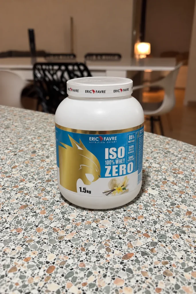Pot d'Iso Zero 100 % Whey Eric Favre vanille 1,5 kg posé sur un plan de travail sombre